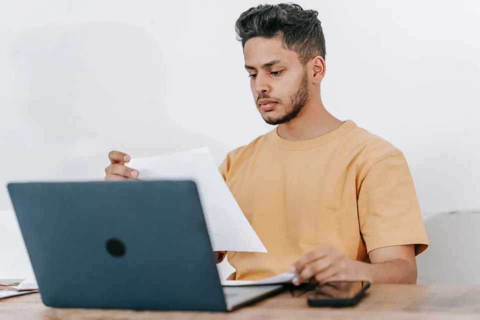 Homem confere papéis ao lado do notebook, em casa