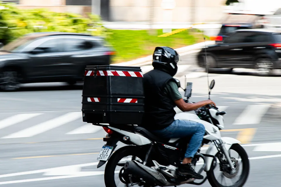 Entregador de moto em trânsito na avenida