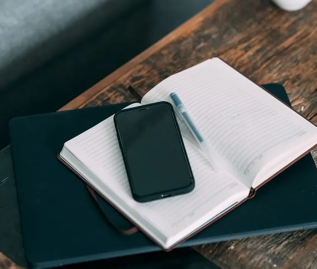 Caderno aberto com um celular e uma caneta sobre a mesa