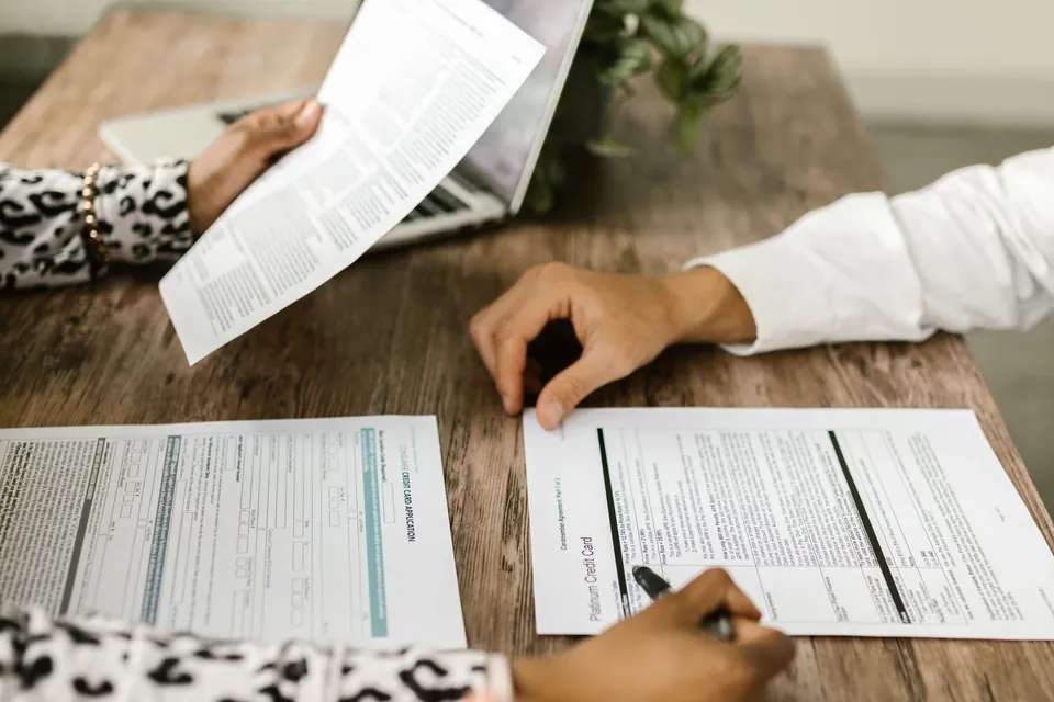 Duas pessoas conferem documentos lado a lado na mesa