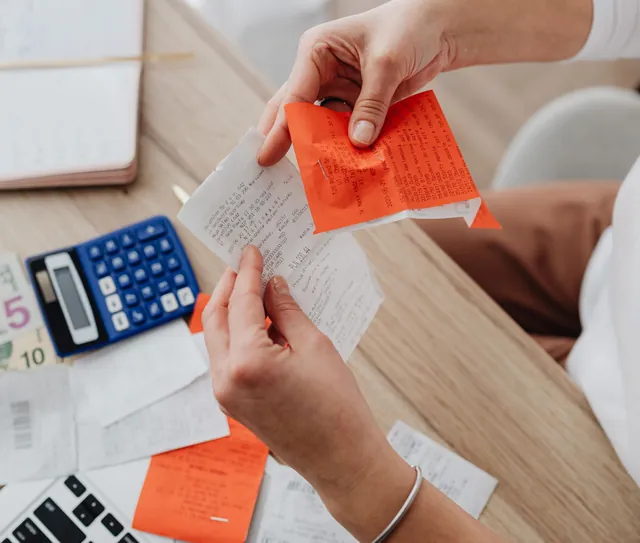 Mãos conferem recibos ao lado de uma calculadora