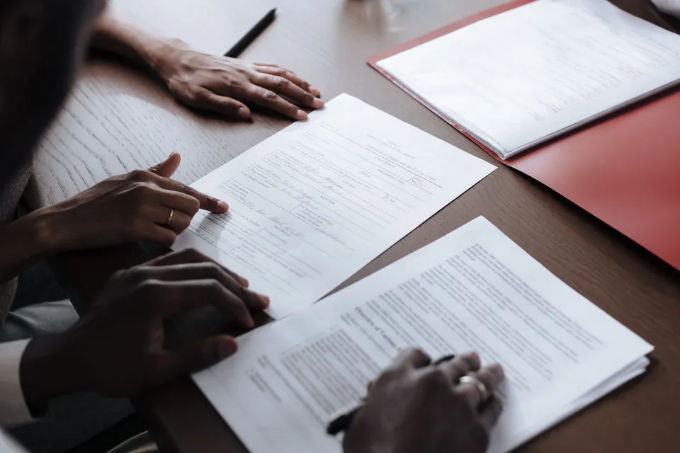 Duas pessoas conferem documentos e uma pasta sobre a mesa