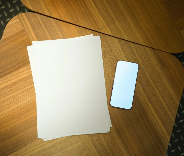 Folhas em branco e um celular sobre a mesa de madeira