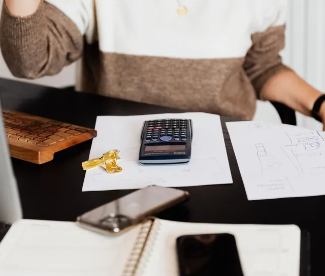 Calculadora, papéis e caneta sobre a mesa de trabalho