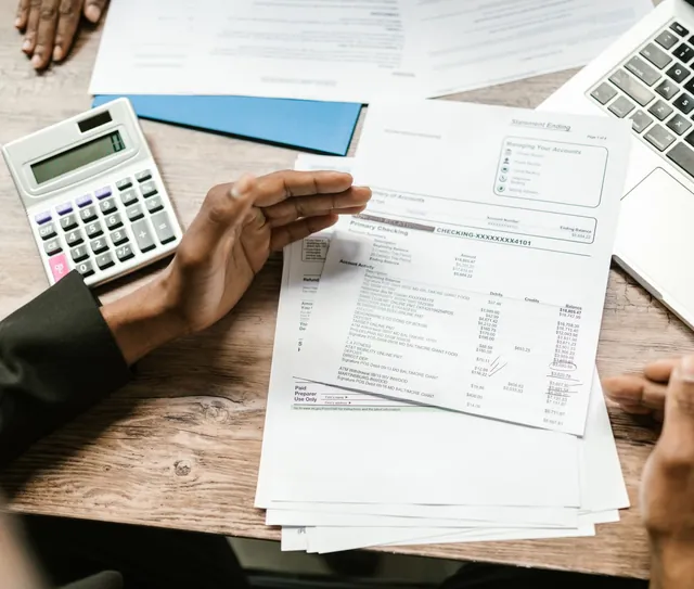 Mãos conferem extratos ao lado de uma calculadora e de um notebook