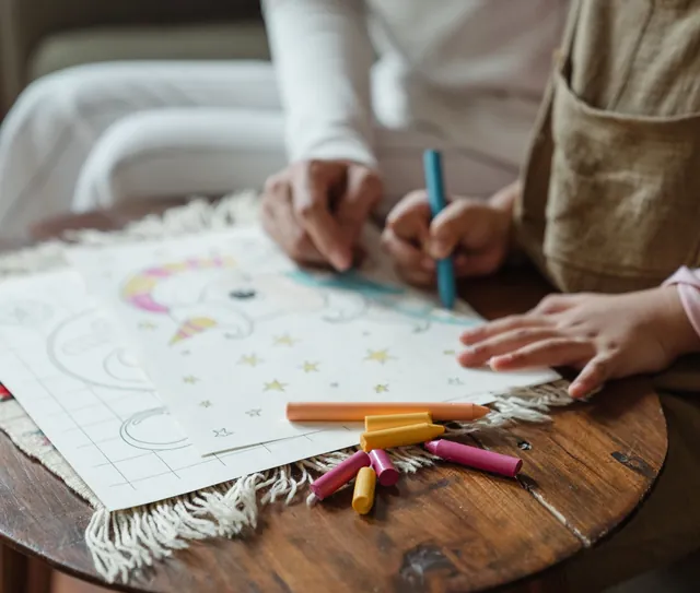 Adulto e criança pintam desenhos juntos à mesa