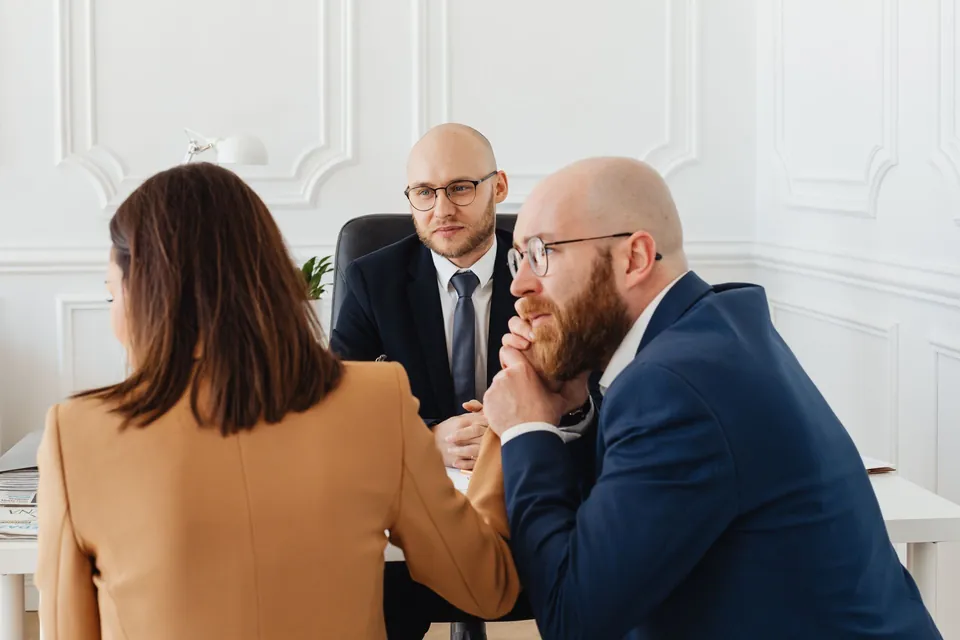 Advogado conversa com dois clientes à mesa do escritório