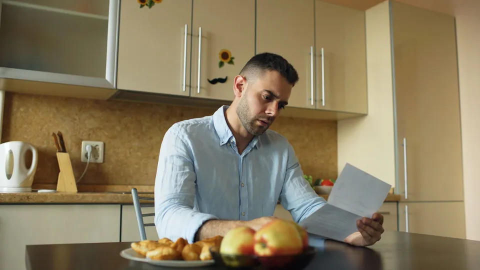 Homem lê um documento à mesa da cozinha