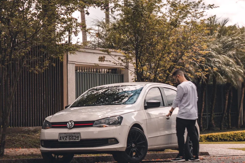 Homem ao lado de um carro popular estacionado na rua