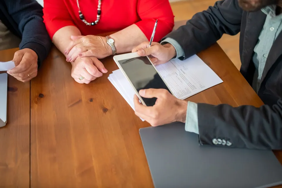 Mãos de três pessoas sobre documentos e um tablet, durante uma reunião