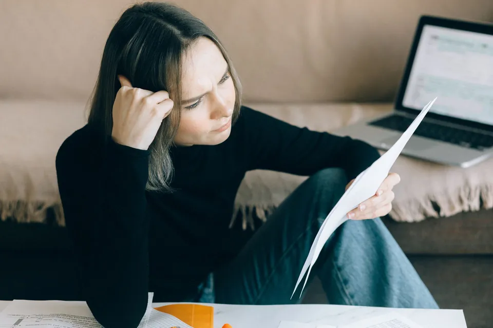 Mulher confere papéis ao lado do notebook, em casa