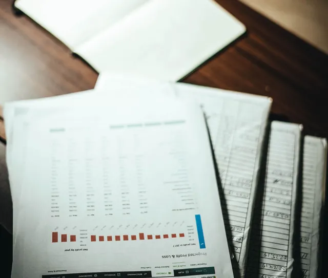 Documentos e um caderno sobre a mesa, ao lado de uma xícara