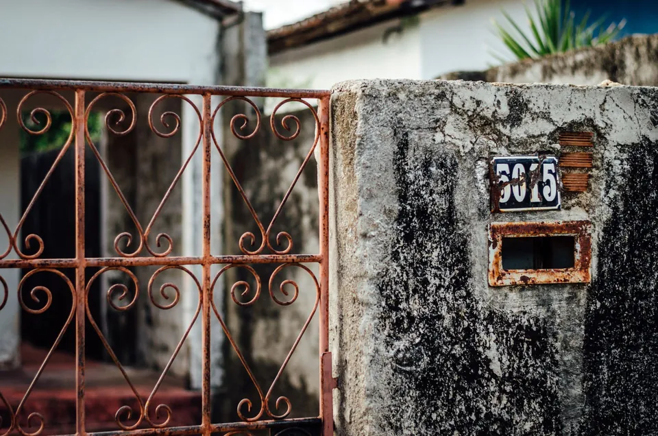 Portão de ferro enferrujado e muro de casa em rua de bairro