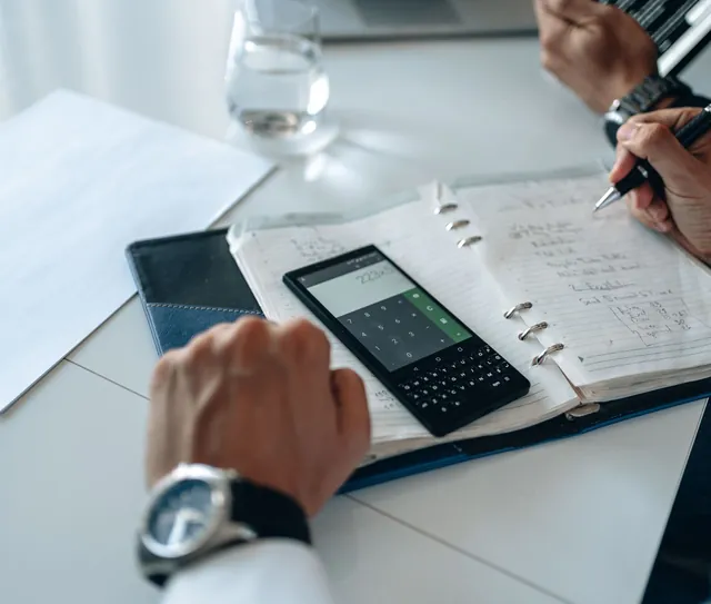 Mãos usam calculadora ao lado de uma agenda e papéis