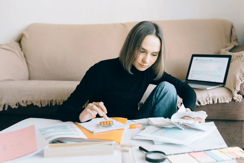 Mulher organiza papéis e contas ao lado do notebook, em casa