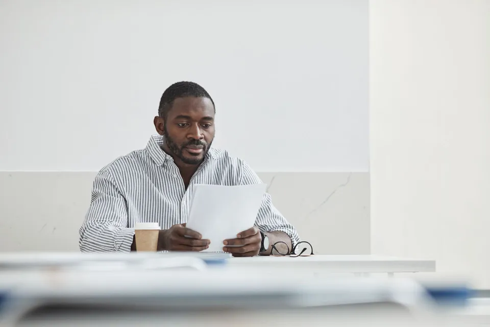 Homem lê com atenção uma folha de papel à mesa