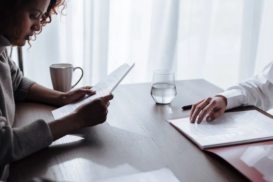 Duas mulheres conferem documentos à mesa