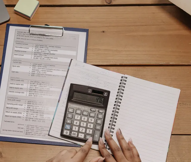Mãos usam uma calculadora ao lado de documentos e de um caderno