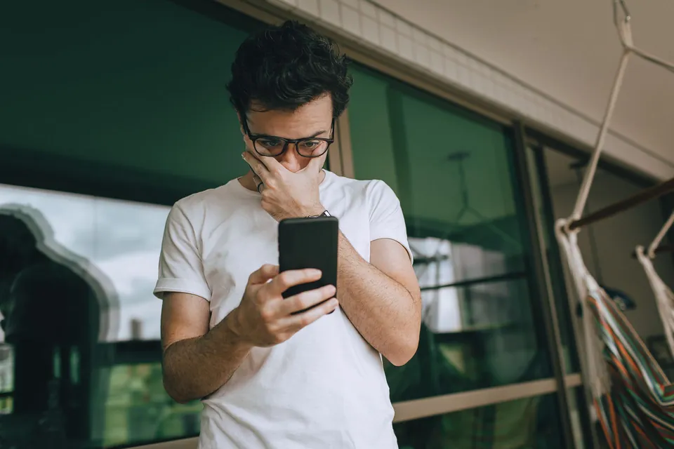 Homem confere o celular com preocupação