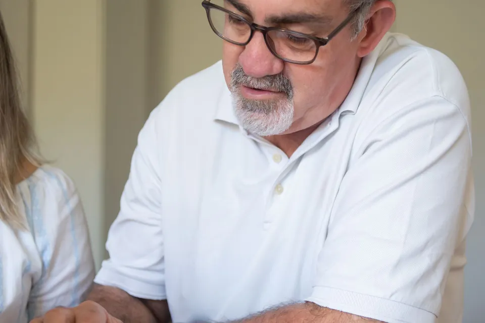 Homem confere um documento e o celular à mesa