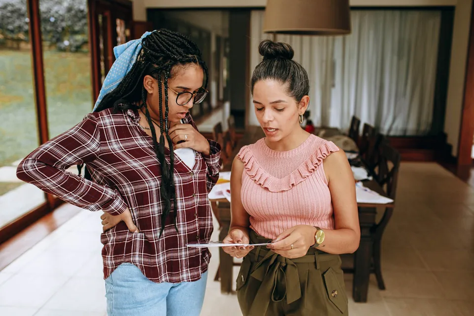 Duas mulheres conferem juntas um documento na sala de casa