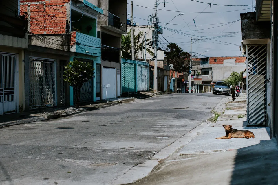 Rua de bairro com casas de tijolo e laje e portões fechados