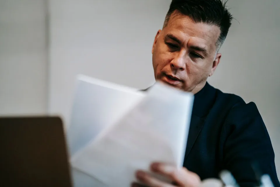 Homem confere as páginas de um contrato impresso sentado na sala de casa