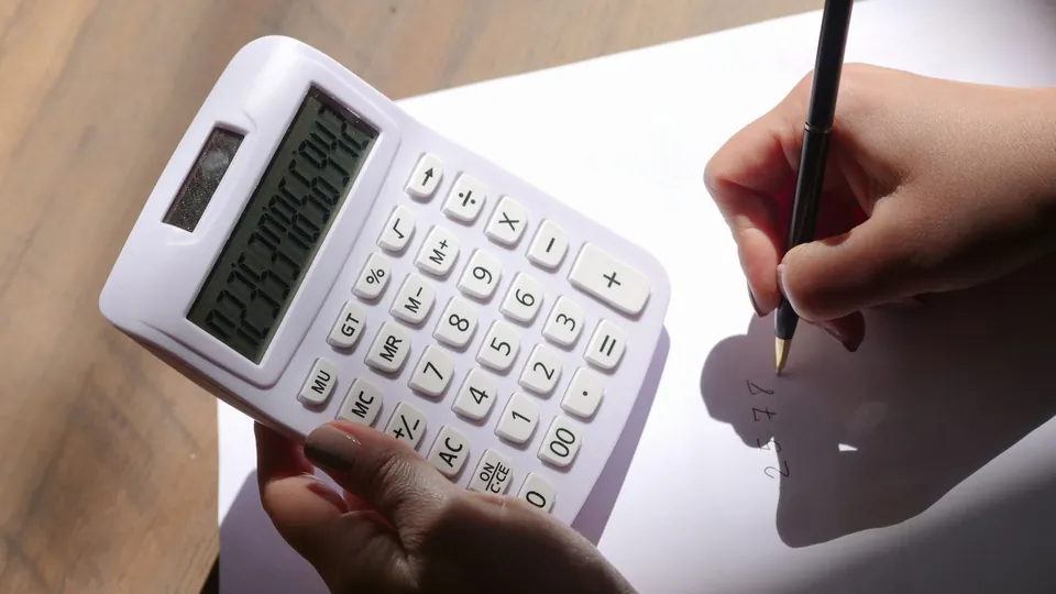Mãos fazem a conta numa calculadora simples e anotam o valor no papel