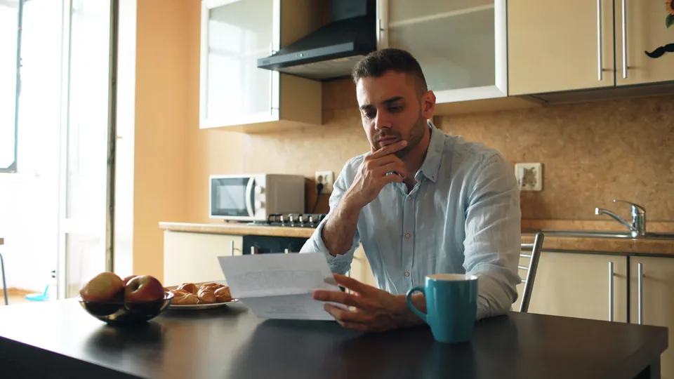 Homem lê uma correspondência à mesa da cozinha