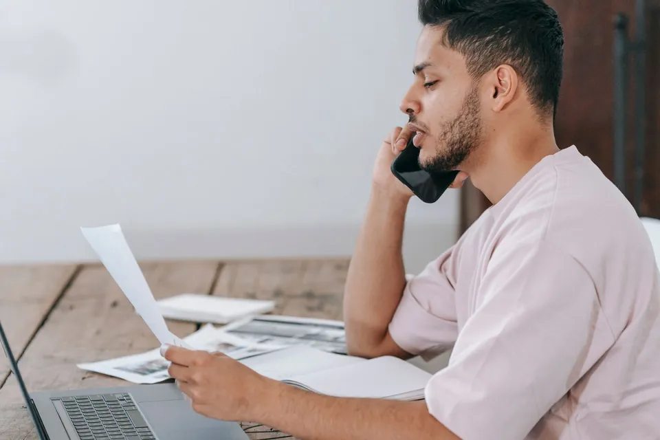 Homem fala ao telefone enquanto confere um documento