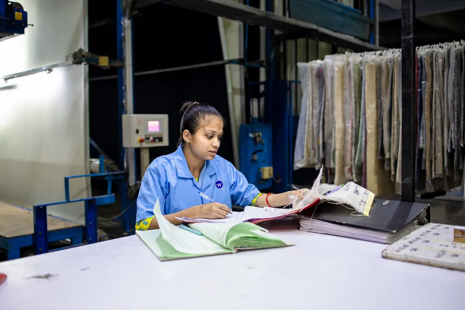 Trabalhadora de uniforme confere anotações na mesa de trabalho